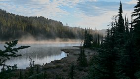 Aerial view of mist rising from a tranquil alpine lake bordered by dense evergreen forest. - Powered by Shutterstock - Get 15% off with code: PIKWIZARD15