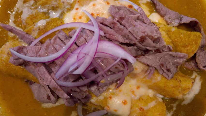 Close-up of a rich Oaxacan dish featuring enchiladas covered in savory mole, garnished with tender shredded beef, cheese, and fresh red onion, served during Guelaguetza festivities.