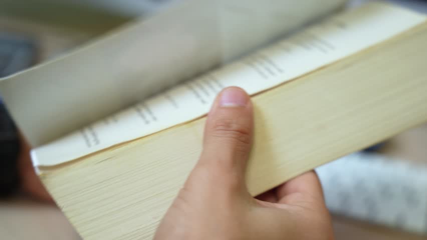 Close-up of hand flipping through book pages in motion. Great for education, research, learning, or literary visuals.
