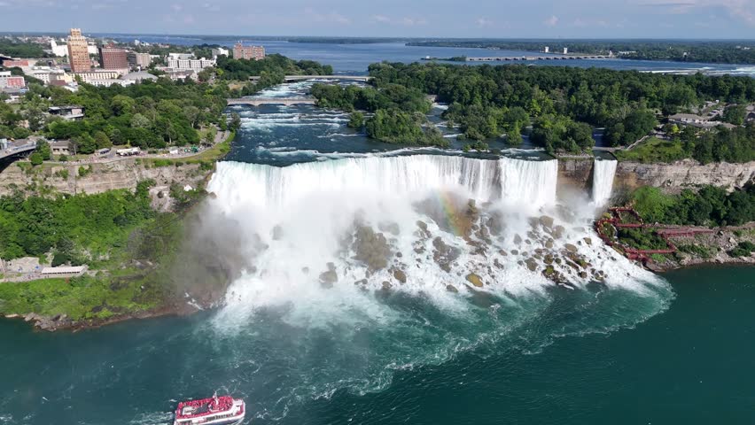Drone glides sideways along American and Bridal Veil Falls, showcasing Niagara Falls State Park beside them and flocks of birds flying near the rushing water