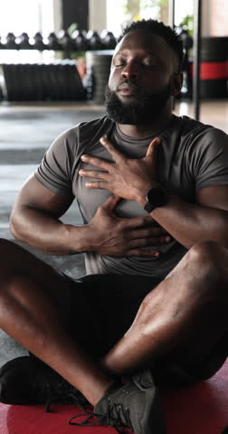 Vertical video: African American man placing hands on torso breathing for focus on gym mat. Meditation, wellness, fitness, mindfulness, relaxation, strength, vertical video