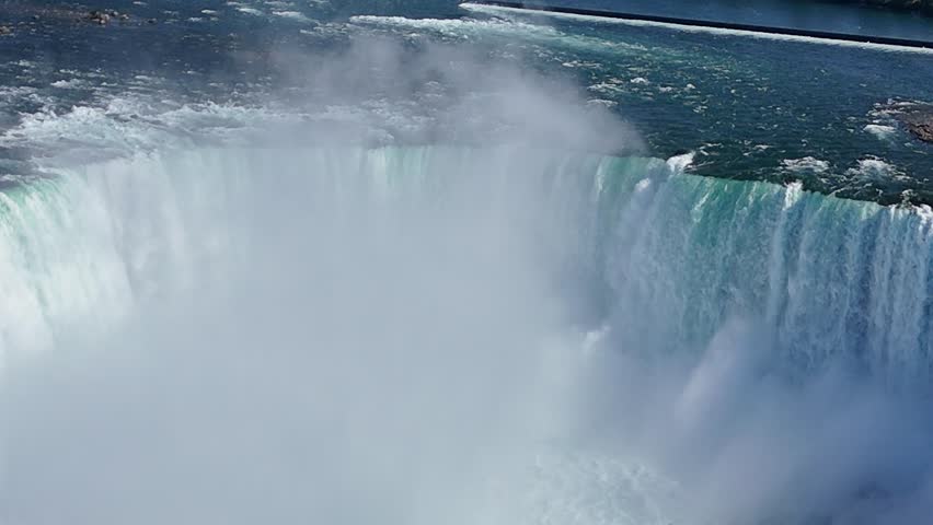 Drone pulls back from the top of Horseshoe Falls, panning down to reveal powerful currents from the edge to the base as the Maid of the Mist cruise ship approaches through the mist