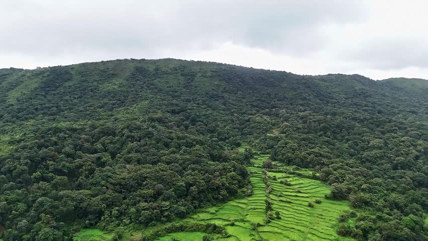 An epic aerial panoramic view of lush mountains,farmlands and a small village covered in mist amidst western ghats forest during winter at Karnataka India