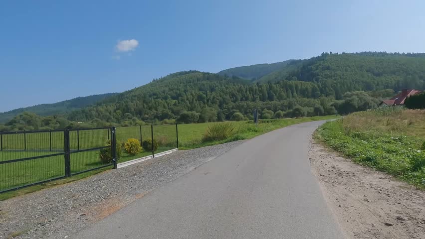 POV cycling along narrow mountain road through fields and forest in Beskid Zywiecki, southern Poland, on sunny day