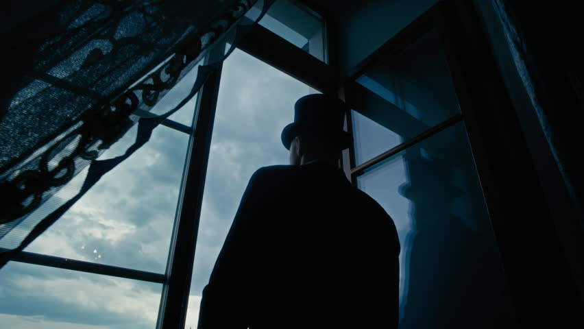 Lowkey back-view shot of vintage-styled man in formal attire adjusting his cylinder hat with gloved hands as he standing by window, gazing thoughtfully at clear blue sky beyond