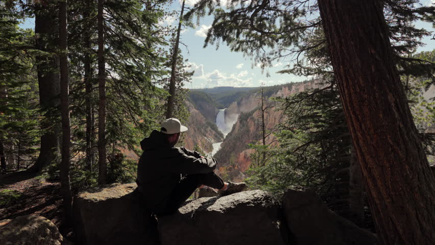 Tourist sitting with stunning and breathtaking view of the magnificent Lower Falls in Yellowstone National Park, capturing incredible and unparalleled beauty of nature in beautiful state of Wyoming