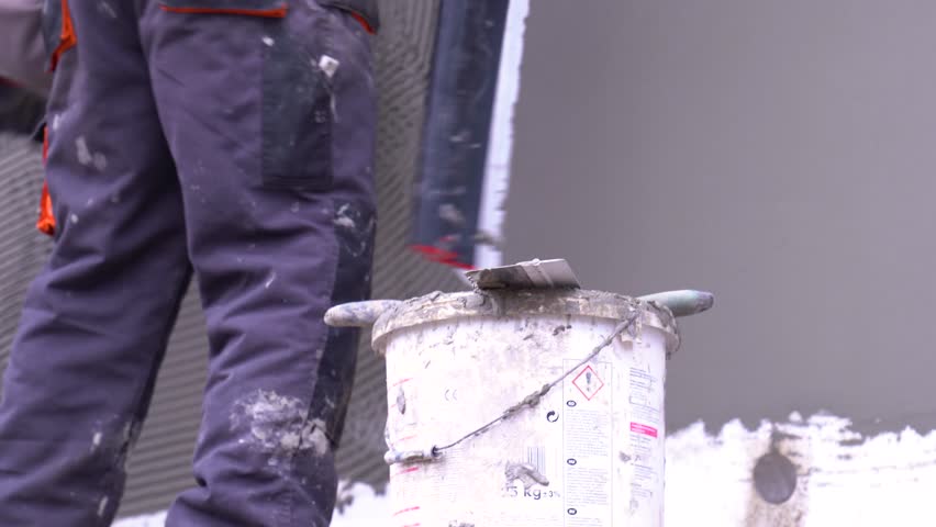 Worker finishes smoothing outer cement layer along building wall surface