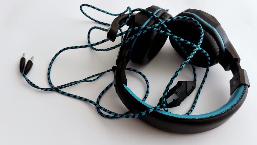 Close-up of hands connecting a 3.5mm audio jack to black and blue over-ear headphones. Crisp white backdrop, braided cable detail-tech meets tactile clarity