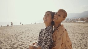 Young women enjoy romantic moments on a sandy beach, embracing and kissing, creating cherished memories together against a picturesque backdrop of hills and buildings - Powered by Shutterstock - Get 15% off with code: PIKWIZARD15