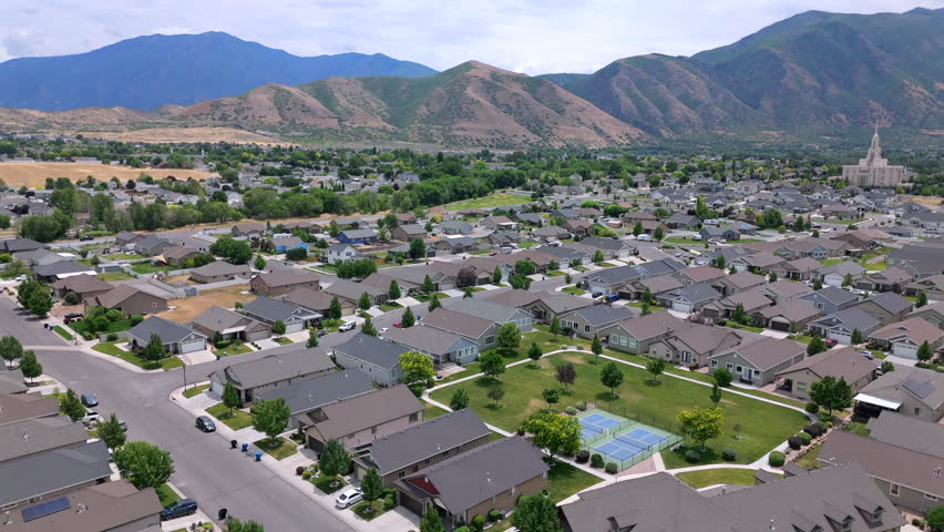 An absolutely stunning aerial footage captures a picturesque USA suburban neighborhood that is beautifully surrounded by majestic mountains, perfectly showcasing the lovely homes and vibrant greenery