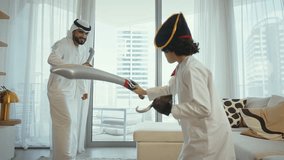 Happy arab family, father in kandura, mother in hijab, and son in pirate costume, enjoying time together, playing pirates with gold coins on the floor of their modern living room - Powered by Shutterstock - Get 15% off with code: PIKWIZARD15