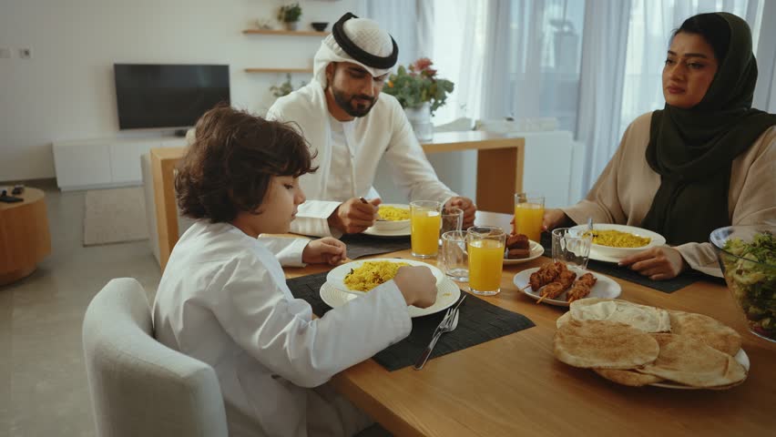 Multigenerational muslim family sharing warm meal together, sitting around dining table, enjoying traditional arabic cuisine with smiling interaction and familial connection