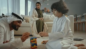 Happy family scene unfolds in a modern living room, an emirati father and son bond over colorful building blocks while the mother, wearing a hijab, relaxes on the sofa. - Powered by Shutterstock - Get 15% off with code: PIKWIZARD15