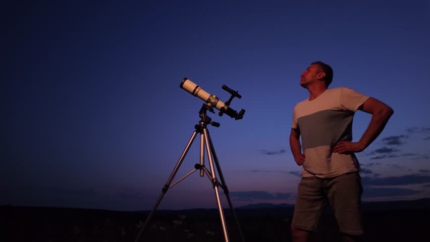 Amateur astronomer using telescope for watching stars, Moon, planets and other celestial objects from a field in nature.	