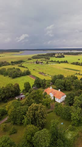 A vertical video captures the timeless charm of Saare Manor, with its historic architecture surrounded by open fields and tall trees, as soft natural light enhances the peaceful countryside setting.