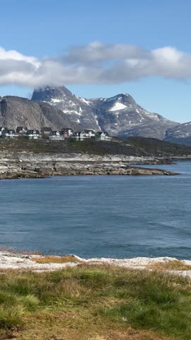 A serene coastal view in Greenland with mountains, calm water, and a small settlement by the shore, tc01
