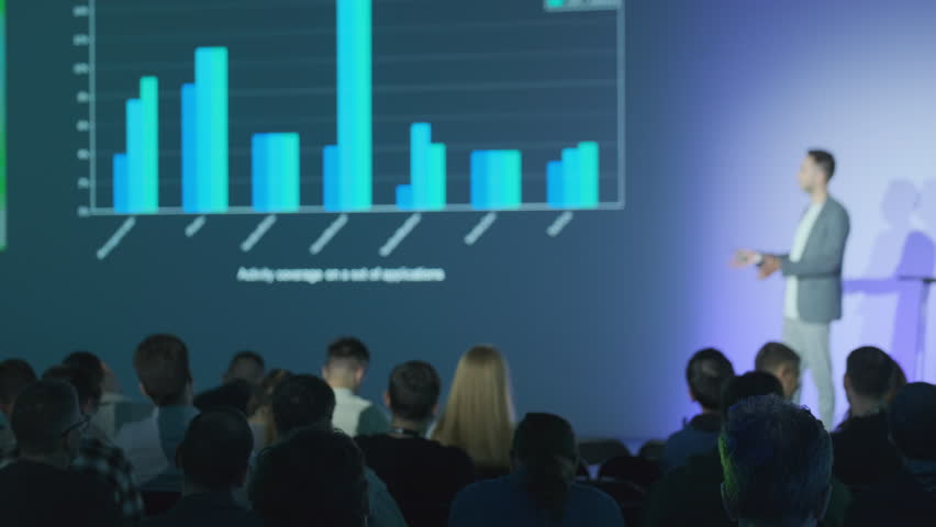 Speaker presenting data visually with graphs to an audience in professional environment