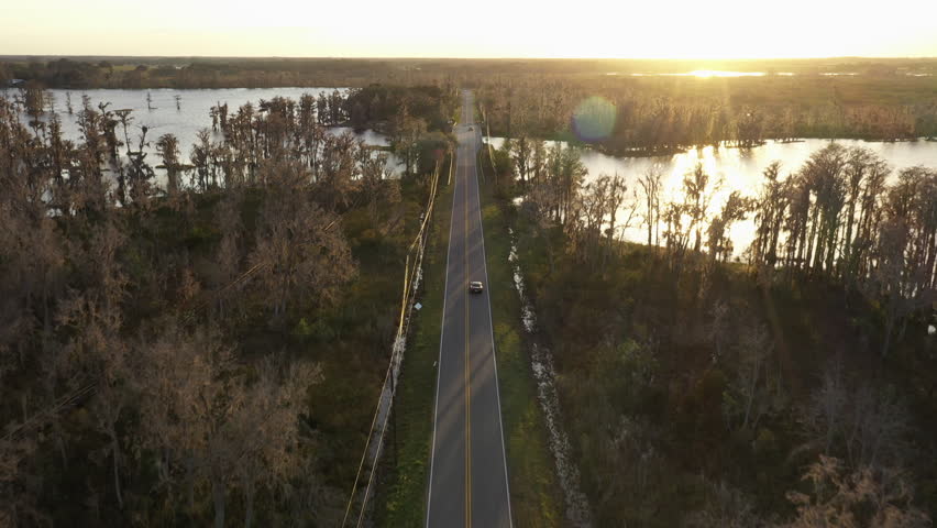 Aerial View Of Car Driving On The Road To The Bridge Over The Lake At Dusk In Clermont, Florida, USA.
