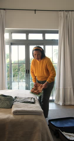 Vertical video: Woman packing suitcase for trip in bedroom and calling on phone, copy space. Travel, organization, lifestyle, casual, home, leisure, vertical video