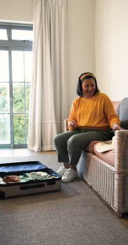 Vertical video: Woman entering bedroom and packing linens and toiletry pouch into open suitcase. Packing, organization, travel, lifestyle, minimalist, domestic, vertical video