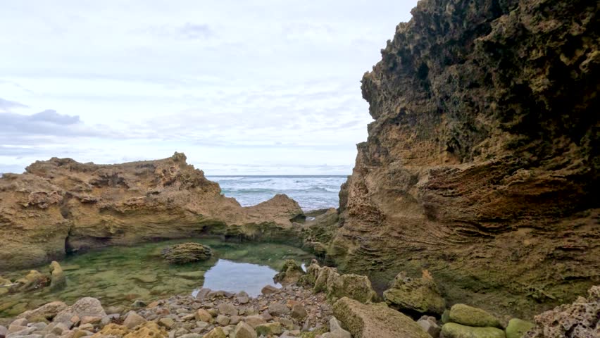 A detailed view of rugged coastal rock formations with natural arches and tidal pools under soft daylight