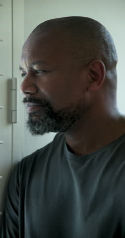 Vertical video: African American man curiously adjusting shutters at home letting light in laughing. Portrait, relaxation, brightness, home, candid, natural, vertical video