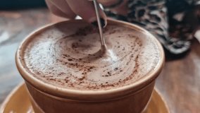 A close-up captures a hand stirring a frothy, coffee-like drink in a mug with a spoon, creating swirls and patterns on the surface - Powered by Shutterstock - Get 15% off with code: PIKWIZARD15
