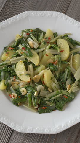 South Croatian Blitva s Krumpirom dish on a white plate. The dish is made with boiled potatoes, swiss chard, garlic, and olive oil. Table spin, vertical video.