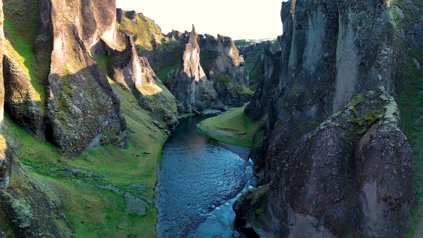 Majestic cliffs rise from the emerald river flowing through Fjadrargljufur canyon in Iceland.