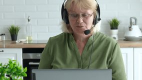 Focused employee wearing headphones with headset, speaking during virtual conference with laptop in kitchen, attending online meeting, participating in video call, looking at computer screen. - Powered by Shutterstock - Get 15% off with code: PIKWIZARD15