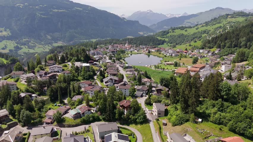 Beautiful idyllic town in Switzerland with lake in center of city. Aerial wide shot. Sunny day in laax, Switzerland. Picturesque landscape with mountains in distance.