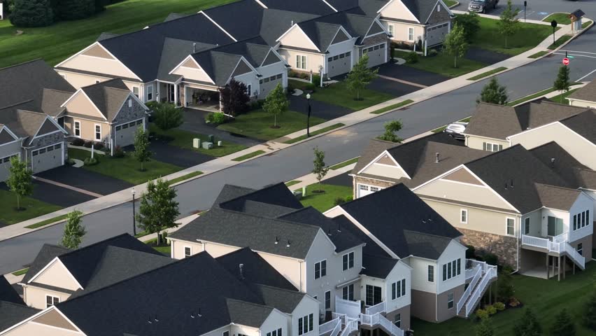 Sunset time in new developed residential area with luxury houses. Aerial lateral shot. American suburb neighborhood with large one family houses and garages. Top down.