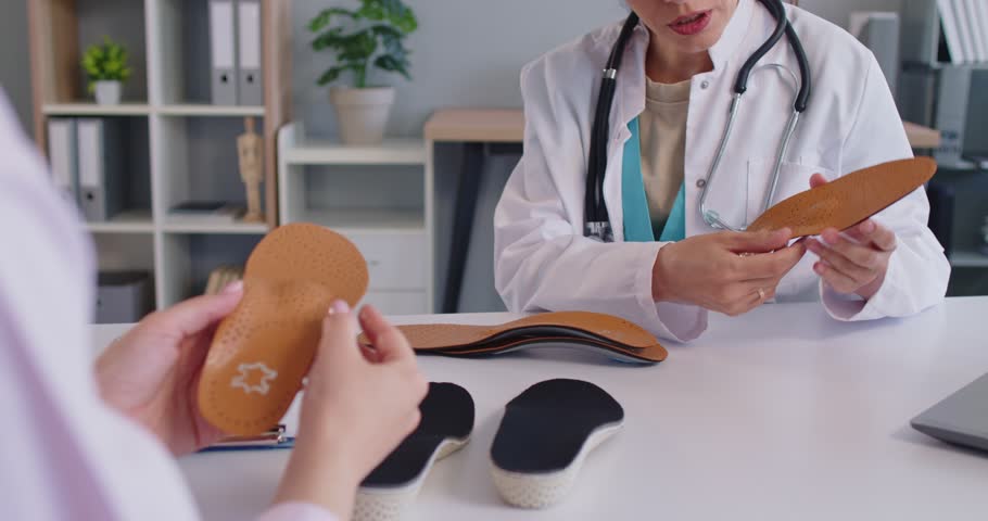 Orthopedists hands holding leather orthotic insole for orthopedic shoes of patient on medical examination in office. Doctor sitting at table with individual orthopaedic inset. Flatfoot support concept