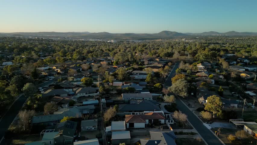 Drone flies above rooftops looking back towards Canberra’s skyline with the iconic tower visible in the far distance.
