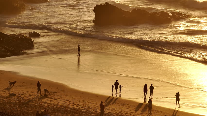 Lisbon, Portugal: Golden sunset casting a warm glow over the beach, with tourists walking along the shore, playing in the sand, and savoring the stunning scenery. Summer travel vacation background