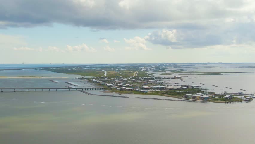 An aerial shot over Caminada Bay looking towards Chenier Caminada near Grand Isle, Louisiana. Footage includes breakwaters, coastal homes, businesses, and a wildlife refuge.