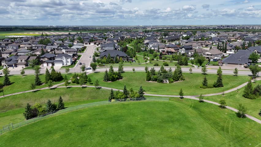 Large green field with a fence in the middle. The field is surrounded by houses and trees