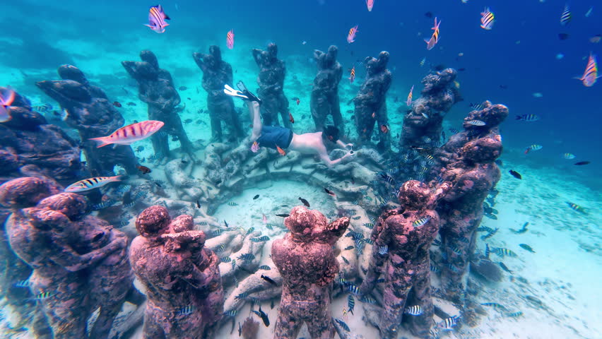 Scuba diver exploring the Bask Nest Underwater sculptures with fishes swimming around in Indonesia.