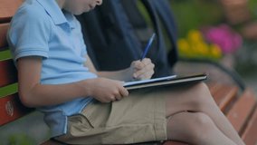 Close-up view of young boy's hands writing homework on lined notebook in park. Light blue polo shirt, khaki shorts, calm summer moment, learning outside. - Powered by Shutterstock - Get 15% off with code: PIKWIZARD15