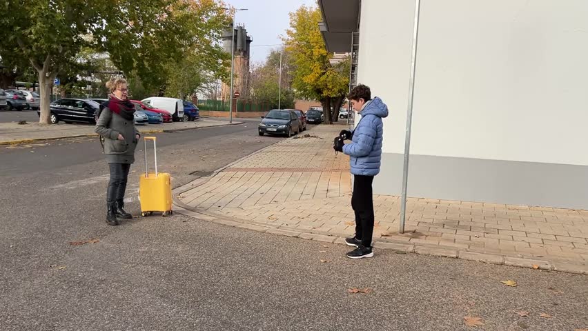 Tourist mother posing for photo in front of Spanish train station while son documents arrival moment