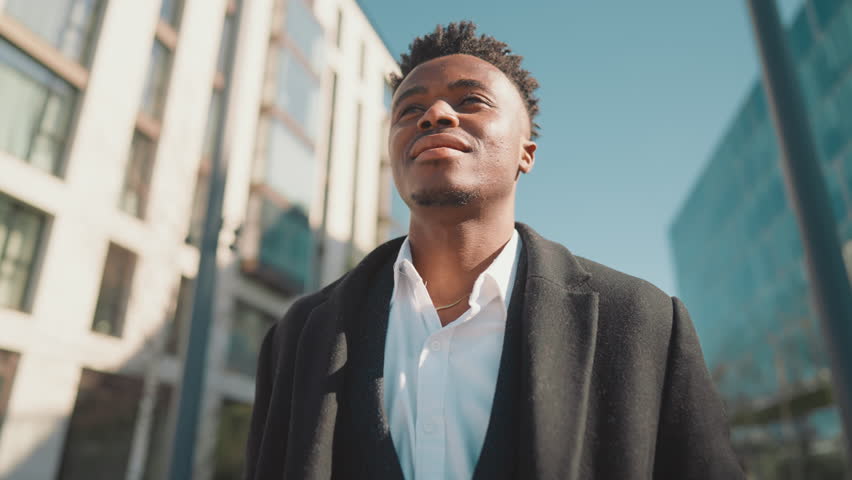 Self-confident black man standing on city street in sunny day, enjoy freedom. African american person inhaling fresh air with aroma of metropolis, dreaming about future successful, young businessman