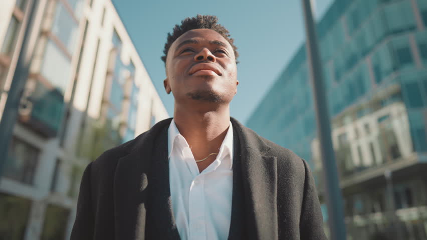 Self-confident black man standing on city street in sunny day, enjoy freedom. African american person inhaling fresh air with aroma of metropolis, dreaming about future successful, young businessman