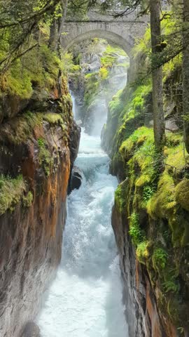 A powerful torrent of white water cascades through a narrow, moss-covered gorge at Pont d'Espagne in the French Pyrenees. The historic stone bridge calmly spans the dramatic, roaring rapids below.

