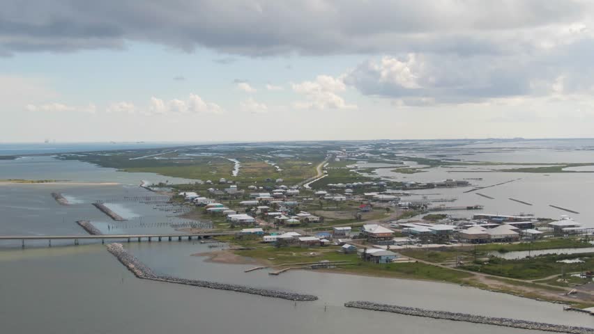 An aerial shot over the bridge looking towards Chenier Caminada in Grand Isle, Louisiana. Footage includes a truck with a trailer, breakwaters, coastal homes, businesses, and a wildlife refuge.