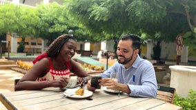 Happy multi-ethnic couple laughing while looking at a smartphone and having breakfast at an outdoor cafe - Powered by Shutterstock - Get 15% off with code: PIKWIZARD15