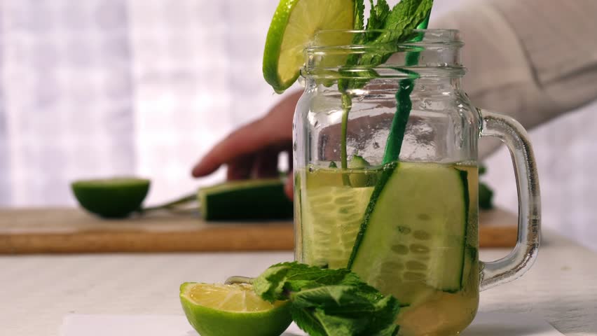 Making healthy cucumber mint and lime refreshing detox drink close up zoom selective shot
