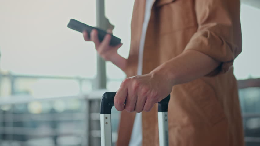 B-roll close-up of Asian male traveler’s hand holding smartphone and suitcase handle at airport terminal – modern travel lifestyle, mobile connectivity, trip preparation journey