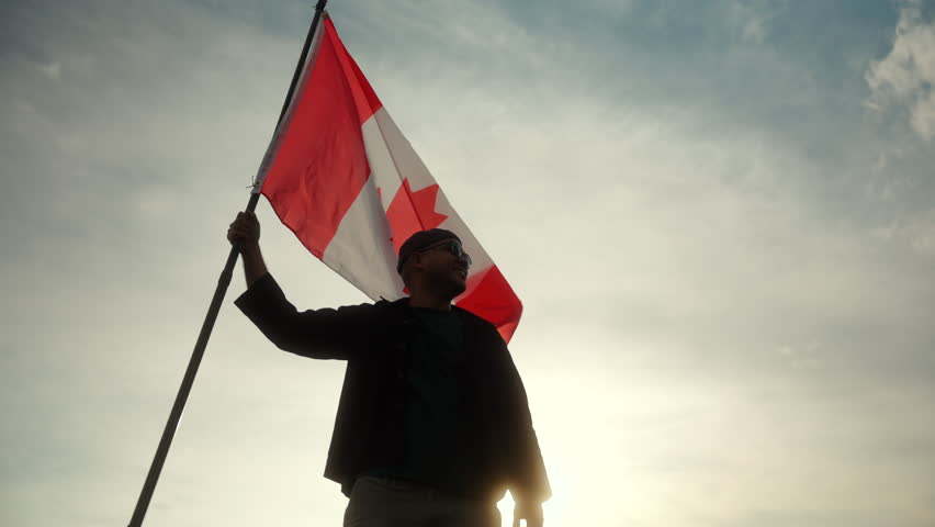 Canadian man standing proudly with holding and raising the Canada flag against blue sky with sunlight. Proud Canadian citizens man holding the Canada flag waving celebration Independence Day.