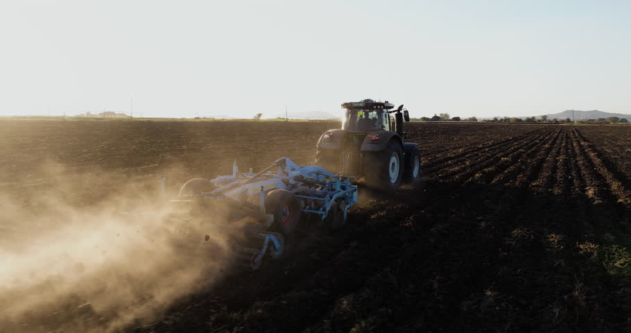 Close-up aerial view of a tractor plowing fields on a large scale vegetable farm. Plowing contributes to climate change and global warming