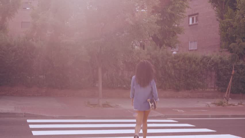 Young woman walking across pedestrian crossing while carrying skateboard